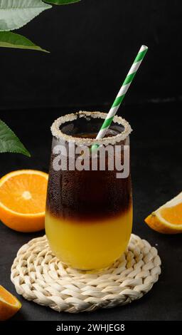 Eiskaffee mit Orangensaft in einem transparenten Glas, erfrischender Hummelkaffee auf dem Tisch, schwarzer Hintergrund Stockfoto