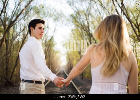 Ein paar Spaziergänge Hand in Hand entlang der Bahngleise, umgeben von üppigen Wäldern Stockfoto