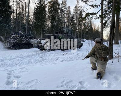 Tapa, Estland. Februar 2024. Ein Soldat kniet im Schnee im Wald neben einem britischen Kampfpanzer Challenger 2 (vorne). Während einer Winterübung in Estland trainieren NATO-Truppen, um die Ostflanke der NATO unter kalten Winterbedingungen zu schützen und zu verteidigen. Die Streitkräfte Frankreichs und Großbritanniens nehmen ebenfalls an der 1. Übung Teil, die vom 15. Februar bis Ende des Jahres läuft. Quelle: Alexander Welscher/dpa/Alamy Live News Stockfoto