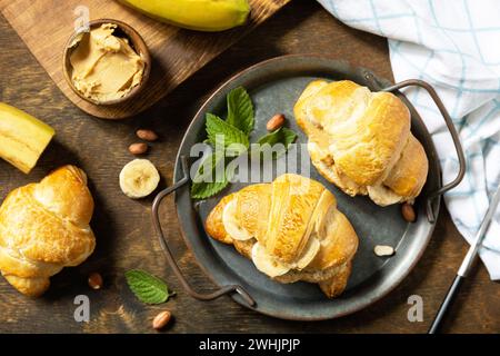 Gesundes Essen Dessert Konzept. Französisches Gebäck. Leckere frisch gebackene Croissants mit Erdnussbutter und Banane auf einem rustikalen Hintergrund Stockfoto