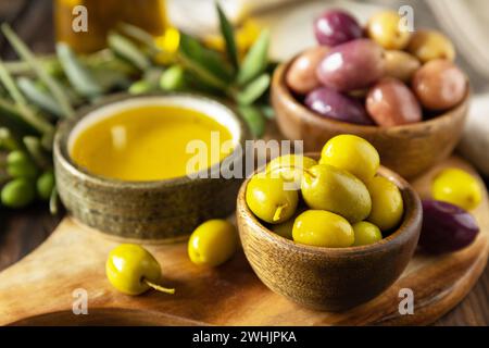 Frisch gepflückte Oliven Beeren in Holzschüsseln und Pressöl auf alten Holzbrettern serviert. Stockfoto