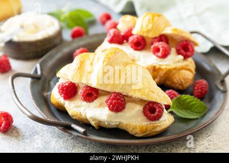 Gesundes Essen Dessert Konzept, französisches Gebäck. Leckere frisch gebackene Croissants mit Frischkäse und Himbeere auf einem Steinhintergrund Stockfoto