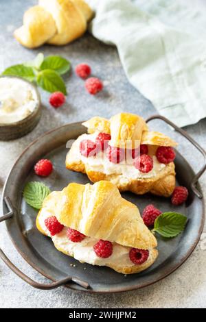 Gesundes Essen Dessert Konzept, französisches Gebäck. Leckere frisch gebackene Croissants mit Frischkäse und Himbeere auf einem Steinhintergrund Stockfoto