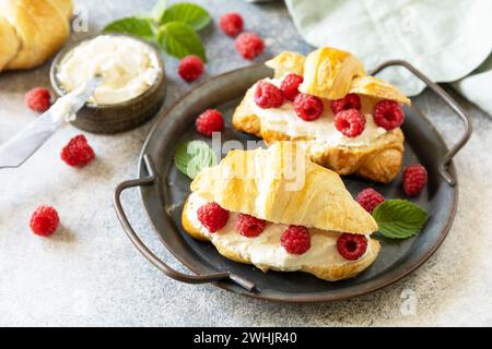 Gesundes Essen Dessert Konzept, französisches Gebäck. Leckere frisch gebackene Croissants mit Frischkäse und Himbeere auf einem Steinhintergrund Stockfoto