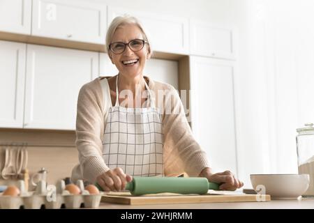 Glückliche Chefkoch-Frau, die Schürze trägt und Gebäck in der Küche macht Stockfoto