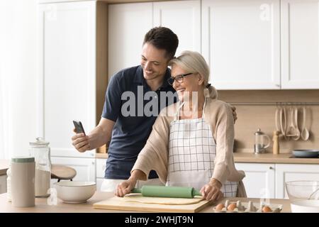Glücklicher erwachsener Mann und ältere blonde Mutter, die in der Küche backen Stockfoto