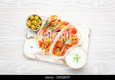 Traditionelles griechisches Gericht Gyros: Pita Brotwickel mit Gemüse, Fleisch, Kräutern, Oliven auf rustikalem Holzschneidebrett mit Tzatziki Stockfoto
