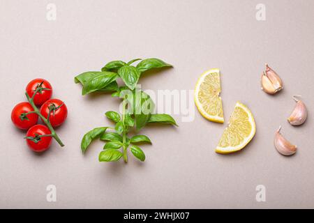 Zusammensetzung mit gesunden Lebensmittelzutaten: Zweig von frischen Kirschtomaten, Basilikumzweig, Knoblauchzehen, Zitronenkeile auf Minimum Stockfoto