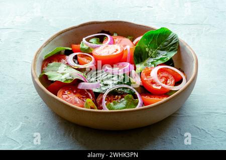 Salat mit Tomaten, frischen Blättern und Zwiebeln, auf Schiefergrund Stockfoto