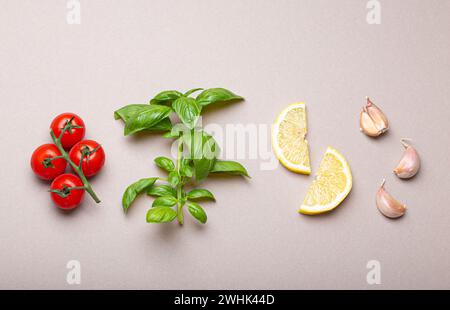 Zusammensetzung mit gesunden Lebensmittelzutaten: Zweig von frischen Kirschtomaten, Basilikumzweig, Knoblauchzehen, Zitronenkeile auf Minimum Stockfoto