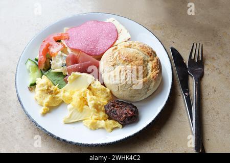 Frühstücksteller mit Brötchen, Rührei, Wurst, Käse und Butter mit Besteck auf einem Steintisch, ausgewählt Stockfoto