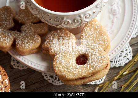 Hausgemachter Linzer-Keks in Form von Huhn in der Nähe einer Tasse Tee, mit dekoriertem Osterei im Vordergrund Stockfoto