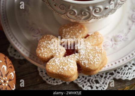 Hausgemachter Linzer-Keks in Form eines vierblättrigen Klees in der Nähe einer Tasse Tee, mit einem Osterei im Vordergrund Stockfoto