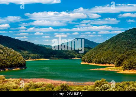 Blauer Himmel mit weißen, geschwollenen Wolken über dem See, umgeben von bewaldeten Bergen und Hügeln Stockfoto
