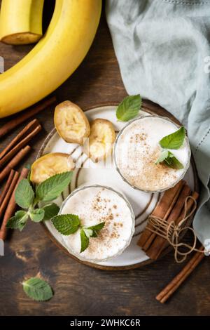 Bananen-Smoothie mit Zimt in Trinkglas auf Holzhintergrund. Entgiftungsmenü. Blick von oben. Stockfoto