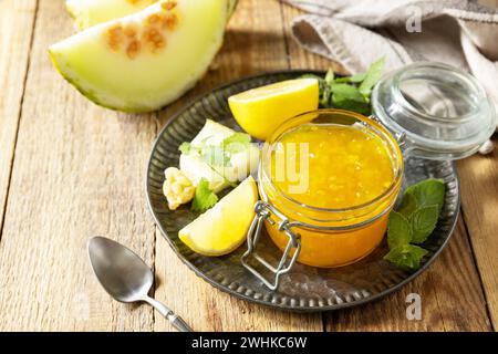 Hausgemachtes Preserve. Süße Melonen- und Zitrusmarmelade oder Gelee in einem kleinen Glas mit frischen Melonenscheiben auf rustikalem Holztisch. Kopie s Stockfoto