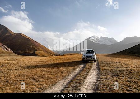 Geländefahrzeug auf einer Strecke zwischen gelben Wiesen, Gletschern im Hintergrund, Lenin Peak, Trans Alay Mountains, Pamir Stockfoto