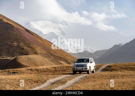 Geländefahrzeug auf einer Strecke zwischen gelben Wiesen, Gletschern im Hintergrund, Lenin Peak, Trans Alay Mountains, Pamir Stockfoto