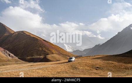 Geländefahrzeug auf einer Strecke zwischen gelben Wiesen, Gletschern im Hintergrund, Lenin Peak, Trans Alay Mountains, Pamir Stockfoto