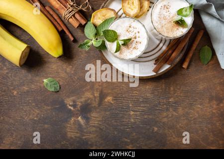 Bananen-Smoothie mit Zimt in Trinkglas auf hölzernem Hintergrund. Entgiftungsmenü. Blick von oben. Kopierbereich. Stockfoto