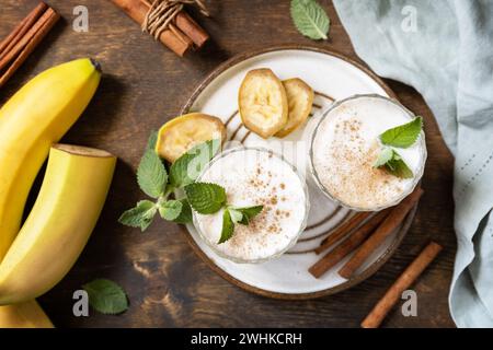 Bananen-Smoothie mit Zimt in Trinkglas auf Holzhintergrund. Entgiftungsmenü. Blick von oben. Stockfoto