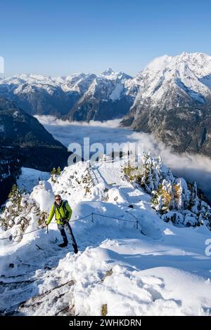 Tourist mit Kamera auf einem Wanderweg, schneebedeckter Gipfel des Jenners mit Aussichtsplattform im Herbst, Blick auf das Wolkenmeer und Watzmann Stockfoto