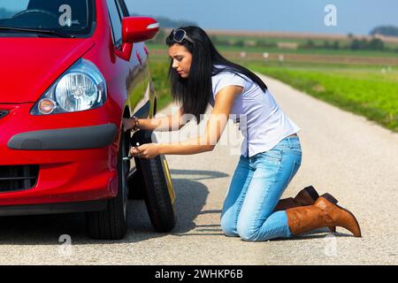 Die junge Frau wechselt einen Reifen an ihrem Auto, eine Reifenpanne Stockfoto