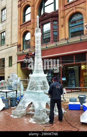 Ottawa, Kanada - 10. Februar 2024: Der Künstler verwendet eine Kettensäge, um eine Eisskulptur des Eiffelturms an der Sparks Street im Rahmen des jährlichen Winterlude-Festivals herzustellen. Das ungewöhnlich warme Wetter im Februar hat es schwierig gemacht, Skulpturen zu erstellen, die langlebig sind, und hat dazu geführt, dass es auf dem Rideau Canal kein Schlittschuhlaufen gibt. Stockfoto