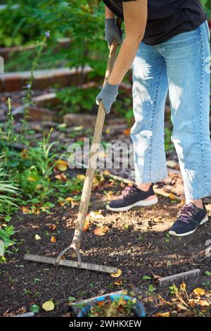 Gärtnerin mit Hut und Schutzhandschuhen, die Erde mit Rechen in ihrem Garten graben Stockfoto