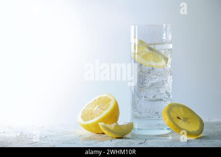 Kohlensäurehaltiges Soda-Wasser mit Eiswürfeln und Zitrone in einem Trinkglas, erfrischendes Getränk vor hellgrauem Hintergrund, Kopierraum Stockfoto