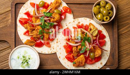 Traditionelles griechisches Gericht Gyros: Pita-Brot mit Gemüse, Fleisch, Kräutern, Oliven auf rustikalem Holzschneidebrett mit Tzatzi Stockfoto