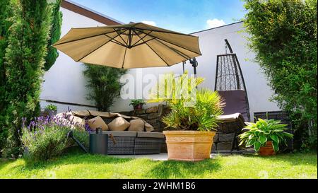 Gartenterrasse mit Loungegruppe und Sonnenschirm in einer Gartenecke mit verschiedenen Pflanzen Stockfoto