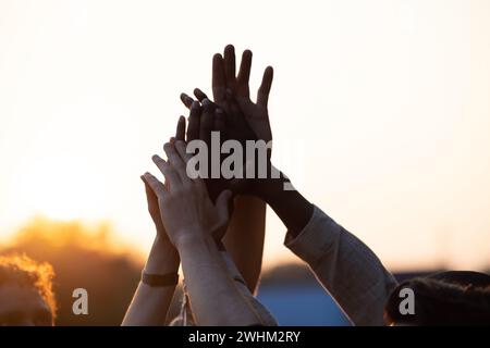 Unity in Silhouette: Multi-Racial Friends High-Fiving und Cheering Against Sunset Sky Stockfoto