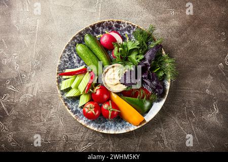 Teller mit Tomaten, Paprika, Rettich und Sellerie, Petersilie, Dill, Koriander, grüne Zwiebeln, rotes Basilikum auf braunem Hintergrund Stockfoto