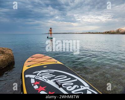 Frau paddelt auf einem Surfbrett unter einem dramatischen Himmel Stockfoto