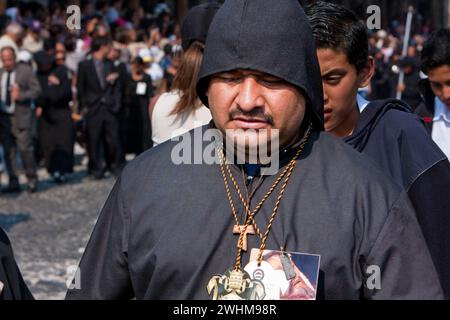 Antigua, Guatemala. Ein schwarzer Cucurucho begleitet einen Karfreitagswagen in einer religiösen Prozession während der Karwoche, La Semana Santa. Stockfoto