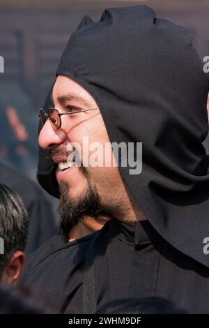 Antigua, Guatemala. Ein schwarzer Cucurucho begleitet einen Karfreitagswagen in einer religiösen Prozession während der Karwoche, La Semana Santa. Stockfoto