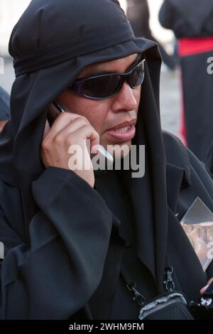 Antigua, Guatemala. Ein schwarzer Cucurucho mit Handy begleitet einen Karfreitagswagen in einer religiösen Prozession während der Karwoche, La Semana San Stockfoto