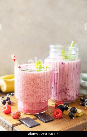 Set aus frischen, verschiedenen köstlichen Milchshakes oder Smoothies mit frischen Beeren auf rustikalem Hintergrund. Himbeeren und schwarze Johannisbeere. Stockfoto