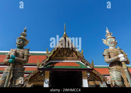 Farbenfroher Eingang zum Gebäude im Großen Palast, Bangkok, Thailand. Aufwändige Golddekoration. Zwei riesige Statuen, die die Tür bewachen. Blue Sky BE Stockfoto