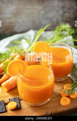 Karottensaft im Glas und frische Karotten mit Blättern auf einem Steintisch. Karotten gesunder Saft für Entgiftung. Gesunder veganer Vegetarier Stockfoto