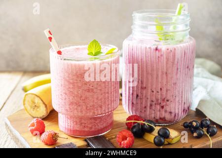 Set aus frischen, verschiedenen köstlichen Milchshakes oder Smoothies mit frischen Beeren auf rustikalem Hintergrund. Himbeeren und schwarze Johannisbeere. Stockfoto