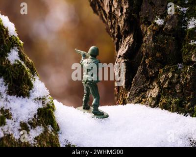 Ein Spielzeugsoldat steht auf einem braunen, grünen, moosigen, verschneiten Baumzweig im gefrorenen, kalten, frostigen Winter. Stockfoto