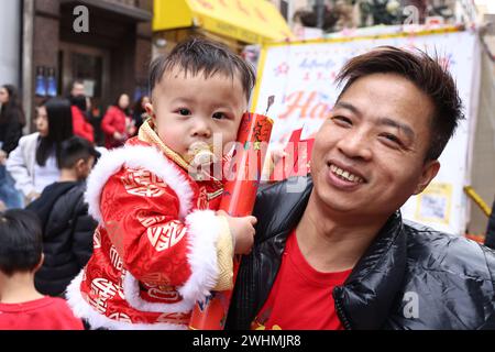 Ein Kind in traditioneller chinesischer roter Kleidung wird vom Vater gehalten, um das chinesische Neujahr in den Straßen von Chinatown in New York, New York, am Samstag, den 10. Februar 2024, zu feiern. Das chinesische Neujahr 2024 ist ein Jahr des Drachen, genauer gesagt Holzdrachen, das vom 10. Februar 2024 beginnt und bis zum 28. Januar 2025 dauert. (Foto: Gordon Donovan) Stockfoto