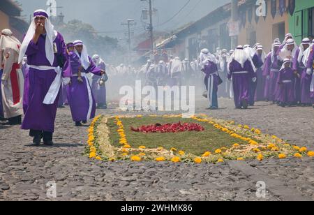 Antigua, Guatemala. Weihrauch erfüllt die Luft, während Cucuruchos in violetten Tuniken den Weg für eine religiöse Prozession während der Karwoche La Semana Santa bereiten. Stockfoto