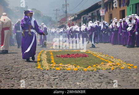 Antigua, Guatemala. Weihrauch erfüllt die Luft, während Cucuruchos in violetten Tuniken den Weg für eine religiöse Prozession während der Karwoche La Semana Santa bereiten. Stockfoto