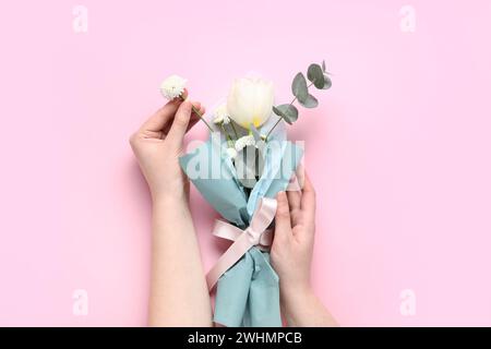 Weibliche Hände mit Ministrauß von schönen Frühlingsblumen in Geschenkpapier auf rosa Hintergrund. Internationaler Frauentag Stockfoto