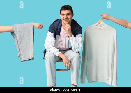 Hübscher junger glücklicher Mann, der auf Stuhl und Händen sitzt und stilvolle Kleidung vor blauem Hintergrund hält Stockfoto