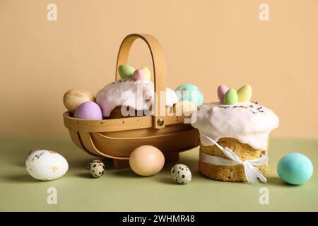 Komposition mit Geschenkkorb, köstlichen Osterkuchen und bemalten Eiern auf farbigem Hintergrund Stockfoto