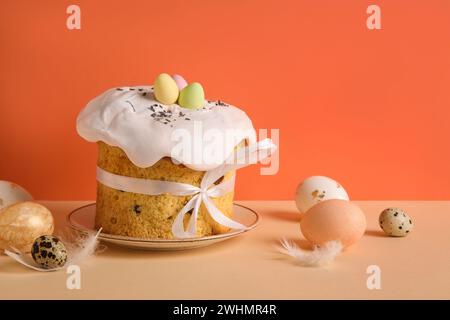 Komposition mit köstlichem Osterkuchen auf Teller und bemalten Eiern auf farbigem Hintergrund Stockfoto